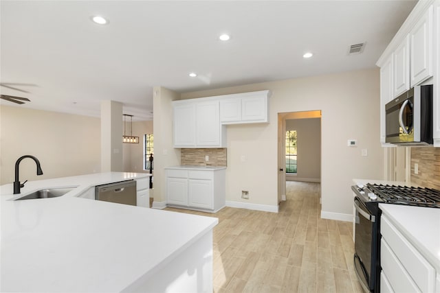 kitchen with appliances with stainless steel finishes, sink, backsplash, white cabinets, and light hardwood / wood-style flooring