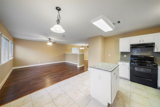 kitchen featuring white cabinets, hanging light fixtures, black gas range oven, light wood-type flooring, and decorative backsplash