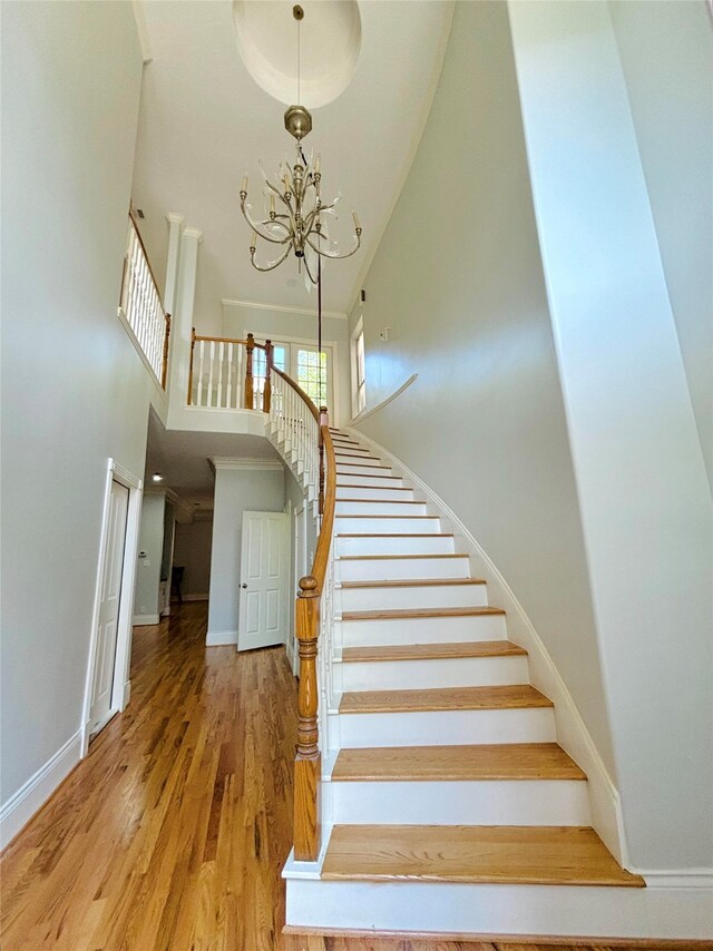 staircase featuring wood-type flooring, a notable chandelier, and a high ceiling