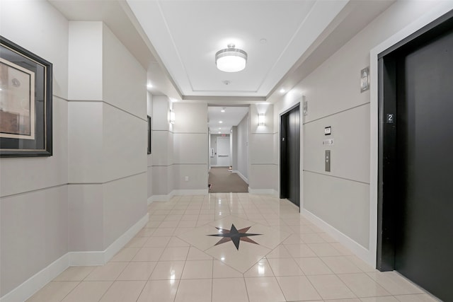 corridor with a tray ceiling, light tile patterned floors, and elevator