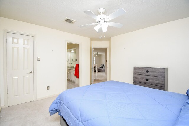 carpeted bedroom with a textured ceiling, ensuite bathroom, and ceiling fan