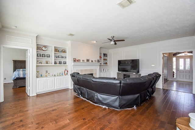 living room featuring a textured ceiling, built in features, dark hardwood / wood-style flooring, a tiled fireplace, and ceiling fan