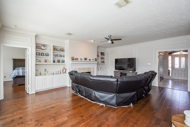 living area featuring built in features, dark wood finished floors, visible vents, and a decorative wall