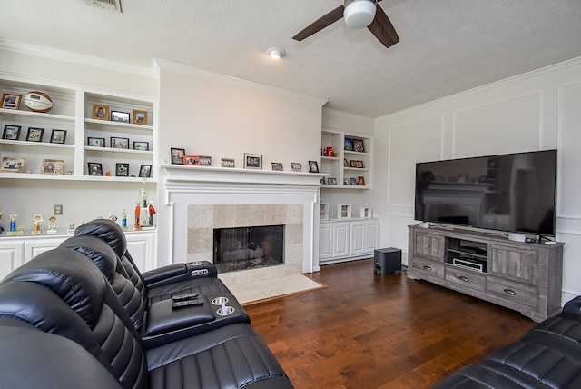 living area featuring a tiled fireplace, dark wood-style flooring, a textured ceiling, built in shelves, and a decorative wall