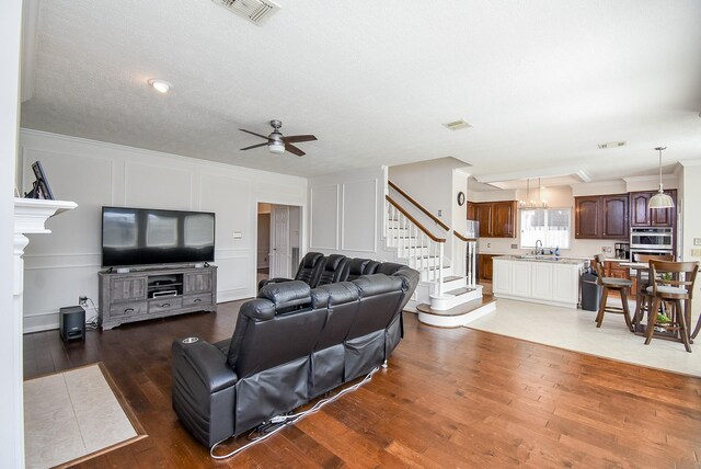 living room with wood-type flooring, sink, ceiling fan with notable chandelier, a textured ceiling, and ornamental molding