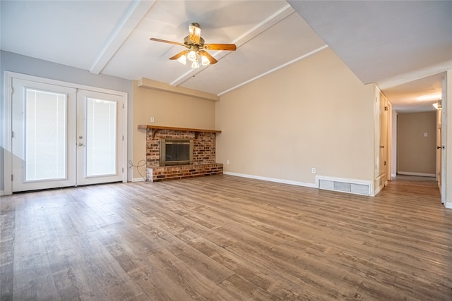 unfurnished living room with a brick fireplace, lofted ceiling with beams, ceiling fan, hardwood / wood-style floors, and french doors