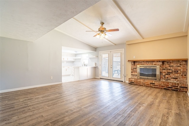 unfurnished living room with ceiling fan, hardwood / wood-style floors, french doors, a fireplace, and vaulted ceiling with beams