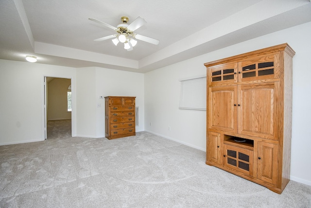 unfurnished bedroom with a raised ceiling, ceiling fan, and light carpet