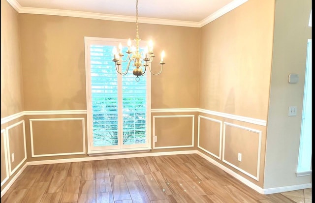 unfurnished dining area with hardwood / wood-style floors, ornamental molding, and a notable chandelier