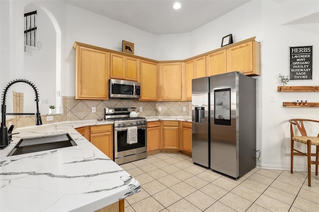 kitchen with sink, stainless steel appliances, tasteful backsplash, light stone counters, and light tile patterned floors