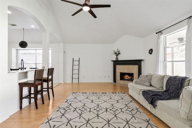 living room with a tile fireplace, ceiling fan, light hardwood / wood-style floors, and vaulted ceiling