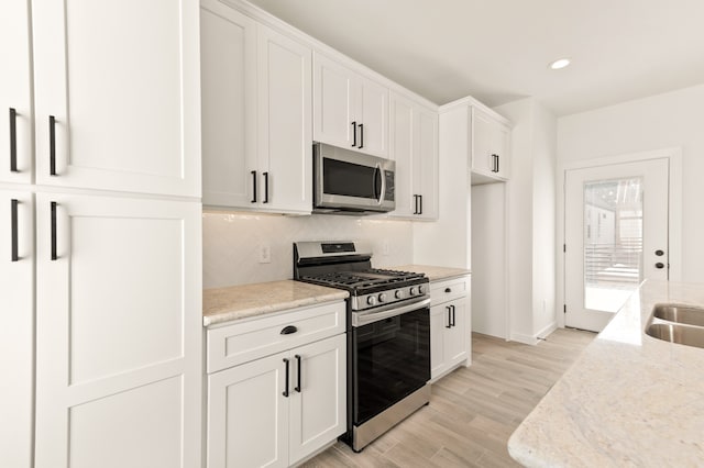 kitchen with light stone counters, white cabinetry, stainless steel appliances, and light hardwood / wood-style flooring