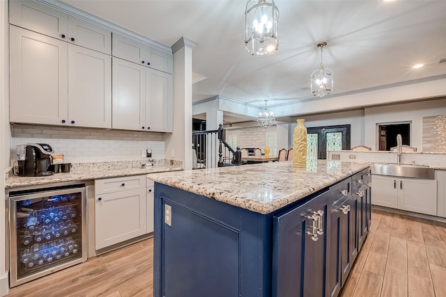 kitchen featuring hanging light fixtures, sink, a kitchen island, beverage cooler, and light wood-type flooring