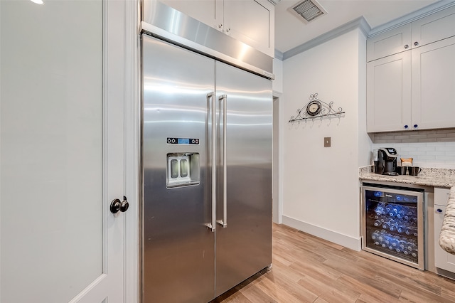 kitchen with light wood-type flooring, wine cooler, light stone counters, stainless steel built in fridge, and ornamental molding