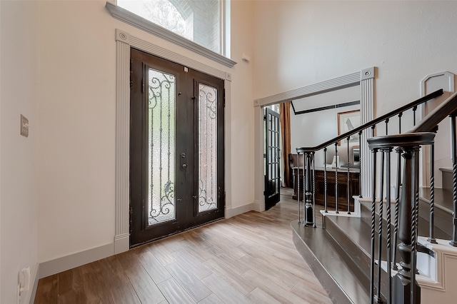 entryway with french doors, light wood-type flooring, plenty of natural light, and a towering ceiling