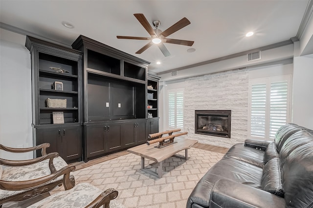 living room with ceiling fan, ornamental molding, light hardwood / wood-style floors, and a stone fireplace