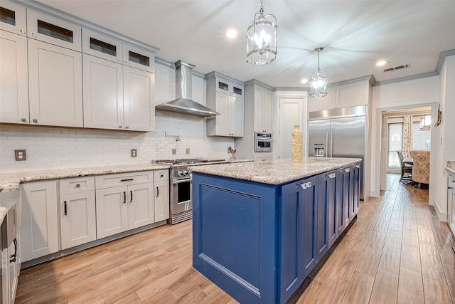 kitchen featuring blue cabinetry, light hardwood / wood-style floors, premium appliances, wall chimney range hood, and hanging light fixtures