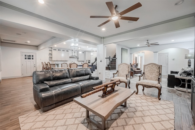 living room with ceiling fan with notable chandelier, light hardwood / wood-style flooring, and ornamental molding