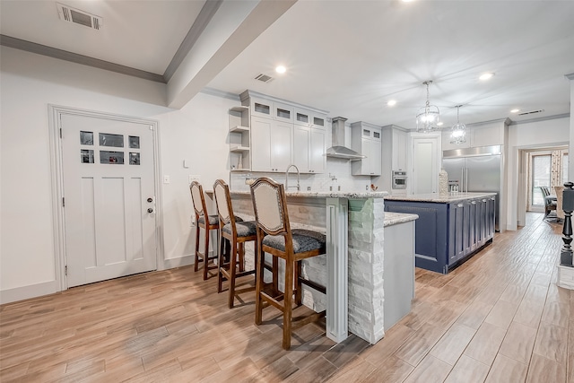 kitchen featuring wall chimney exhaust hood, pendant lighting, blue cabinetry, a kitchen breakfast bar, and stainless steel appliances