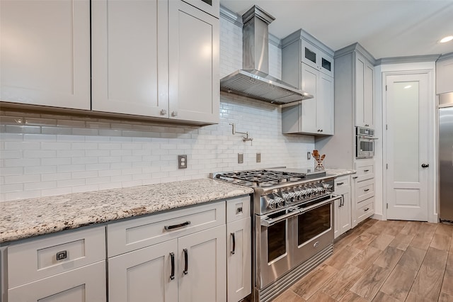 kitchen featuring premium appliances, light hardwood / wood-style flooring, light stone countertops, and wall chimney range hood