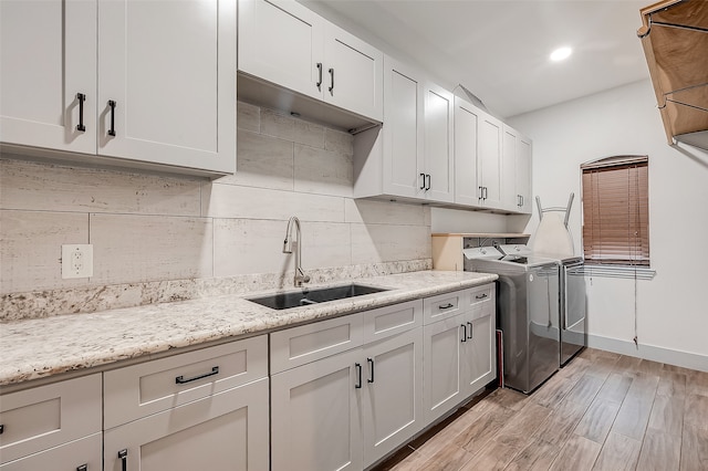 kitchen with independent washer and dryer, white cabinetry, sink, and light hardwood / wood-style flooring