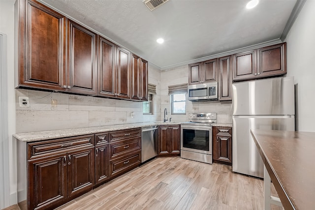 kitchen featuring ornamental molding, appliances with stainless steel finishes, light wood-type flooring, and dark brown cabinets