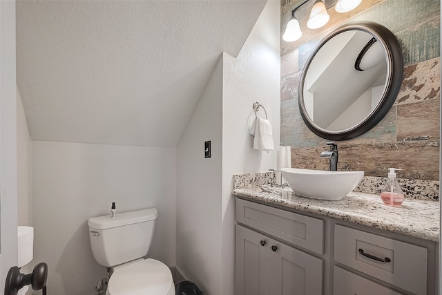 bathroom with lofted ceiling, backsplash, vanity, and toilet