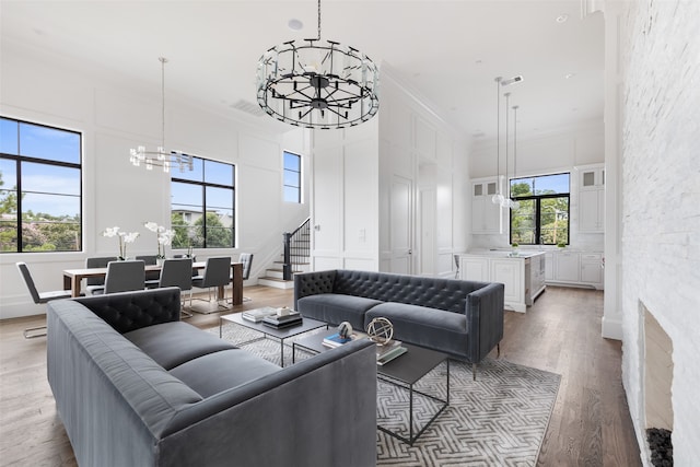 living room featuring a towering ceiling, crown molding, a chandelier, and light wood-type flooring