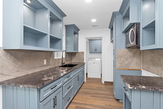 kitchen featuring washer / dryer, decorative backsplash, hardwood / wood-style floors, dark stone countertops, and sink