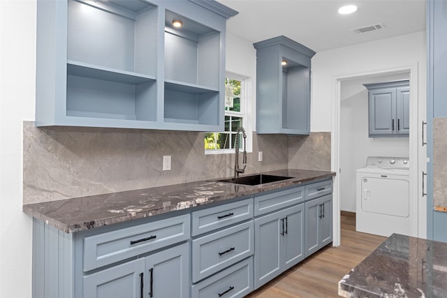 kitchen featuring sink, backsplash, washer / clothes dryer, dark stone countertops, and hardwood / wood-style floors