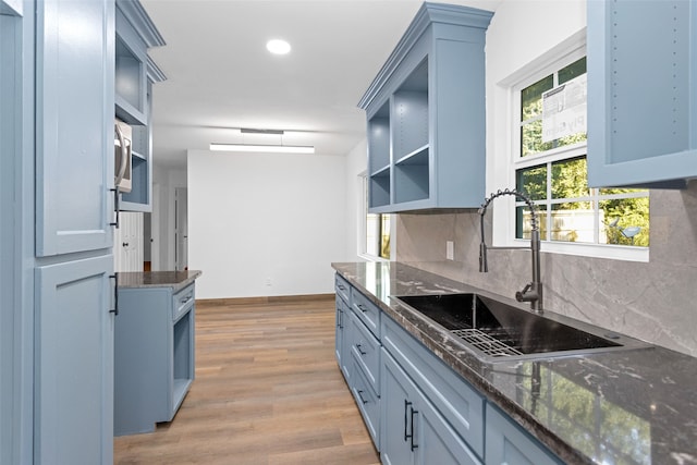 kitchen featuring light wood-type flooring, blue cabinets, sink, and backsplash