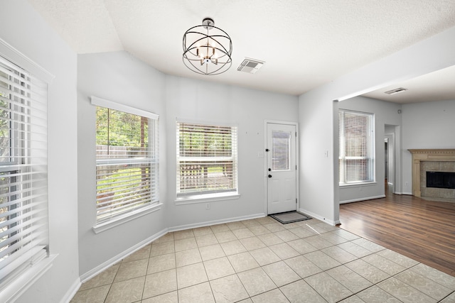 entryway featuring a textured ceiling, an inviting chandelier, light wood-type flooring, and a tile fireplace