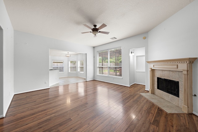 unfurnished living room with hardwood / wood-style flooring, ceiling fan with notable chandelier, a tiled fireplace, and a textured ceiling