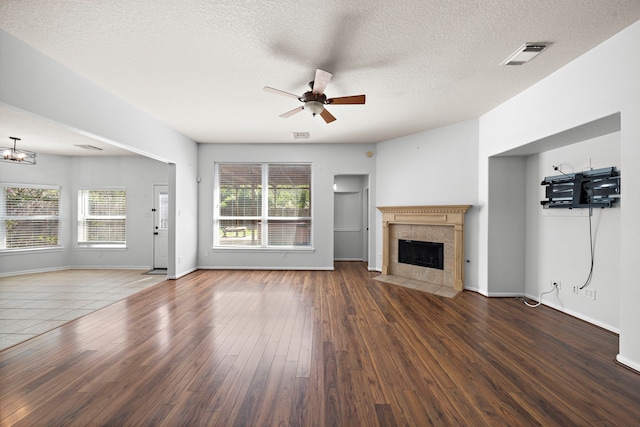 unfurnished living room featuring ceiling fan, a wealth of natural light, a tile fireplace, and dark hardwood / wood-style flooring