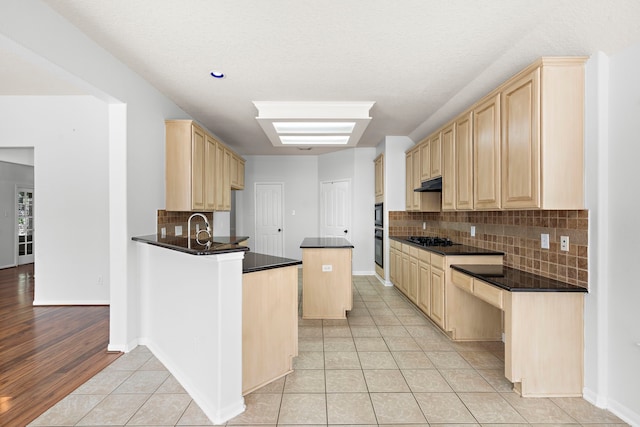 kitchen with a kitchen island, light wood-type flooring, black gas stovetop, light brown cabinetry, and backsplash