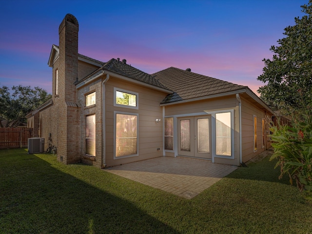 back house at dusk featuring central air condition unit, a patio area, and a lawn