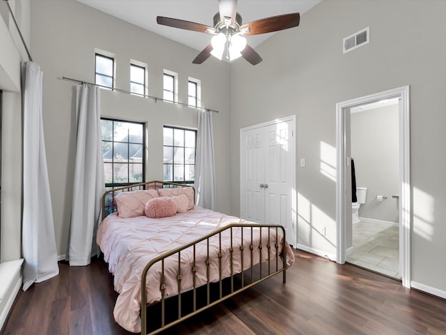 bedroom with ensuite bath, ceiling fan, dark hardwood / wood-style flooring, and a high ceiling