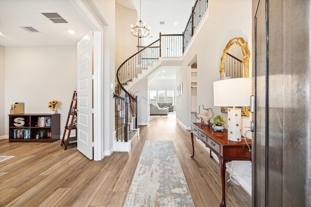 entryway with a notable chandelier, a towering ceiling, and light hardwood / wood-style floors