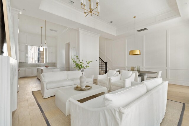 living room with a notable chandelier, crown molding, a tray ceiling, and light hardwood / wood-style flooring