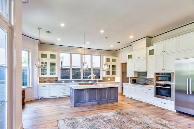 kitchen with a center island, stainless steel appliances, ornamental molding, decorative light fixtures, and light wood-type flooring