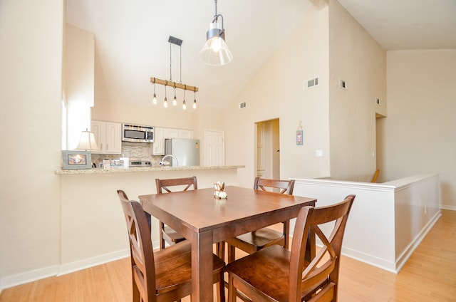 dining area with high vaulted ceiling and light hardwood / wood-style flooring