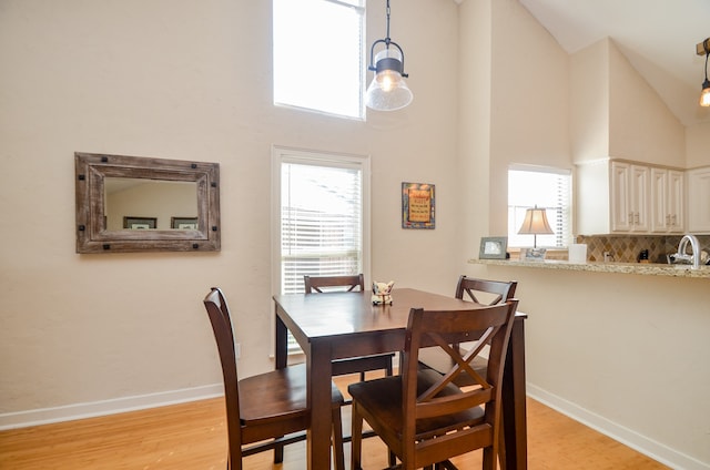 dining space featuring light wood-type flooring, high vaulted ceiling, and sink