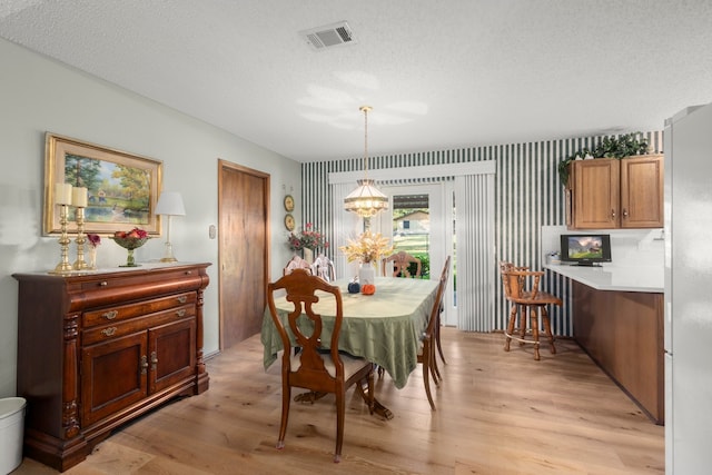 dining room featuring a textured ceiling, an inviting chandelier, and light hardwood / wood-style flooring