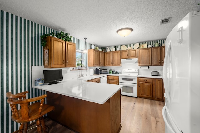 kitchen featuring light wood-type flooring, white appliances, kitchen peninsula, pendant lighting, and a textured ceiling