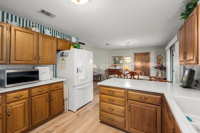 kitchen featuring white fridge with ice dispenser, sink, light hardwood / wood-style flooring, decorative light fixtures, and a textured ceiling