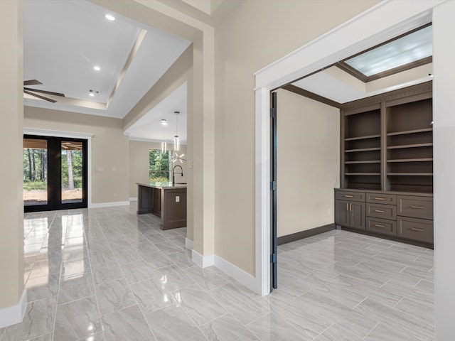 corridor with built in features, sink, ornamental molding, a tray ceiling, and french doors