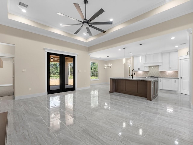 kitchen with an island with sink, sink, white cabinets, light stone counters, and a raised ceiling