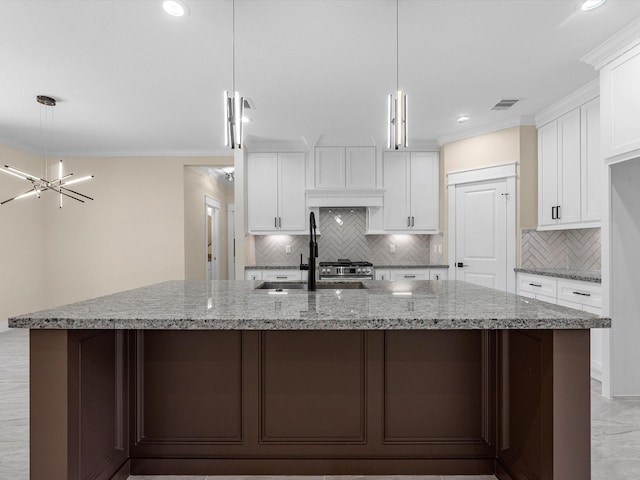 kitchen with pendant lighting, white cabinetry, a large island with sink, crown molding, and light stone countertops