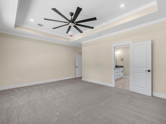 unfurnished bedroom featuring ensuite bathroom, light colored carpet, ornamental molding, and a raised ceiling