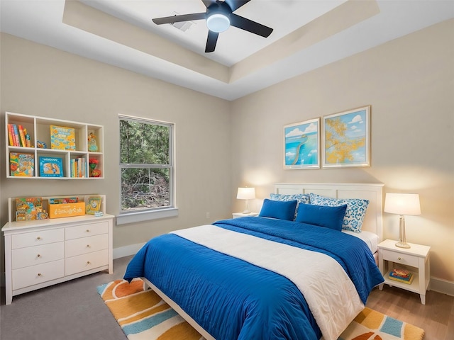 bedroom with ceiling fan, a raised ceiling, and hardwood / wood-style floors